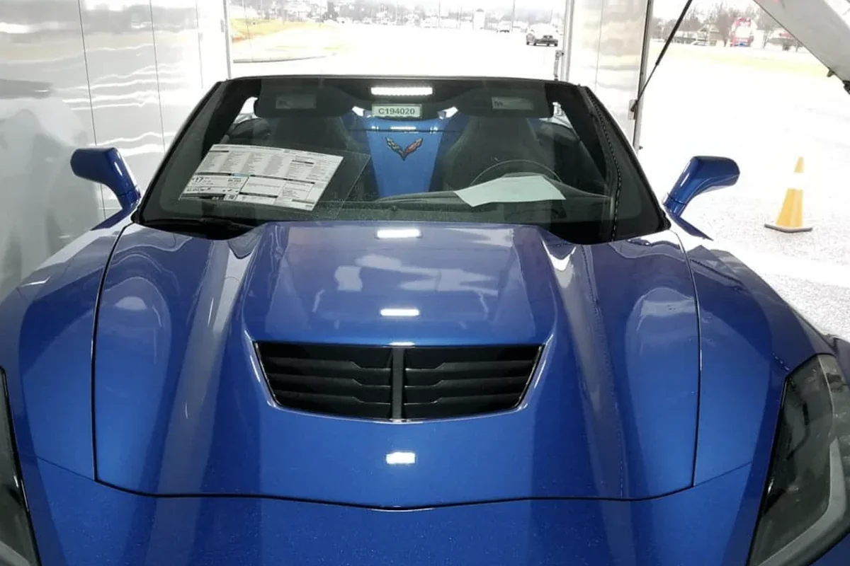 Blue Chevrolet Corvette convertible parked inside an enclosed car transport trailer with the rear door open